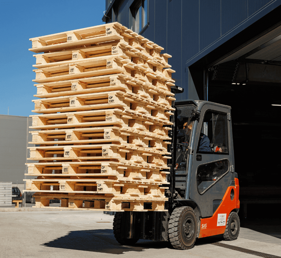 Forklift transporting stacked wooden pallets outside warehouse