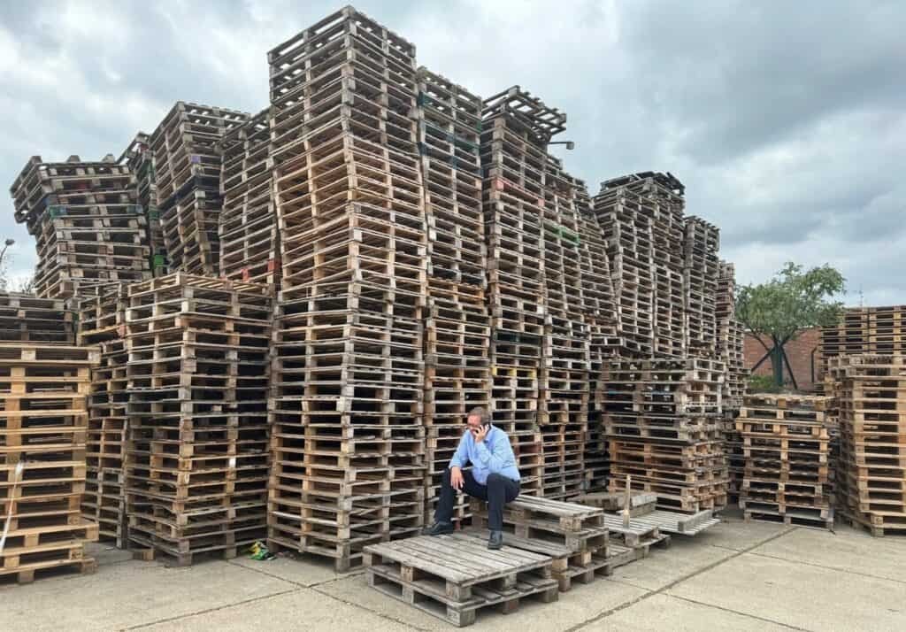 A man sitting in front of a pile of used pallets.